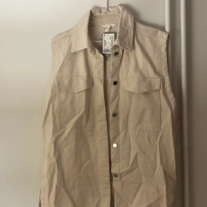 Ny cargo-denimväst - En ny beige denimväst, längre, oversized modell. Prislappen finns kvar. Originell pris 199SEK. Storlek S. 