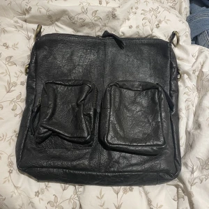 Svart axelremsväska - Ascool svart axelremsväska, mammas gamla. Läderliknande material, vet inte om det är äkta läder eller vilket märke det är. Den är stor till ”ytan” men ganska platt, så den rymmer inte jättemycket.