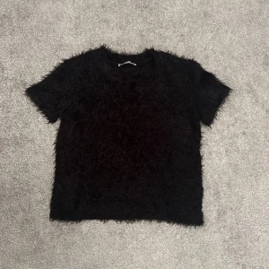 Svart fluffig T-shirt - Denna T-shirt är varm och har en  fluffig material. Den är oanvänd och i bra skick. Tröjan är inte kort, längden slutar precis efter naveln 