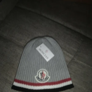 Moncler mössa  - Moncler mössa helt ny grå färg ser liten ut men när Man tar på sig den töjs den ut och blir större ser liten ut bara för den e ny !! Kom för detaljer 