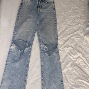 Vida byxor  - Ett par ljusblåa byxor från bikbok med hål vid knäna.