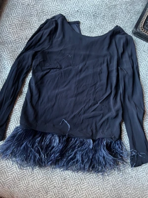 Glansig topp med fjädrar - Superfin! Långärmad mörkblå satintopp med fjädrar längst fram från Thomas Rath.