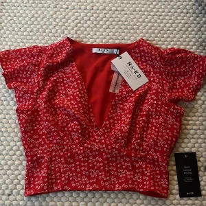 Sommartopp - En röd topp från nakd med små vita blommor på. Passar perfekt till midsommar. Har en fin v-ringning och resår i midjan.