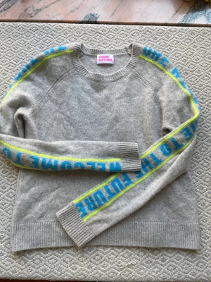 FromFuture grå kashmir tröja med detalj på armarna - Grå kashmir tröja ifrån FromFuture med blåa och gröna detaljer på armarna. Små tecken på användning så som nopper men inget som är jättesynligt enligt mig!