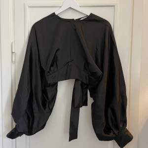 Satinblus med öppen rygg - Svart satinblus med öppen rygg. Kort modell, endast testad. Knytes med band baktill. Perfekt festblus!