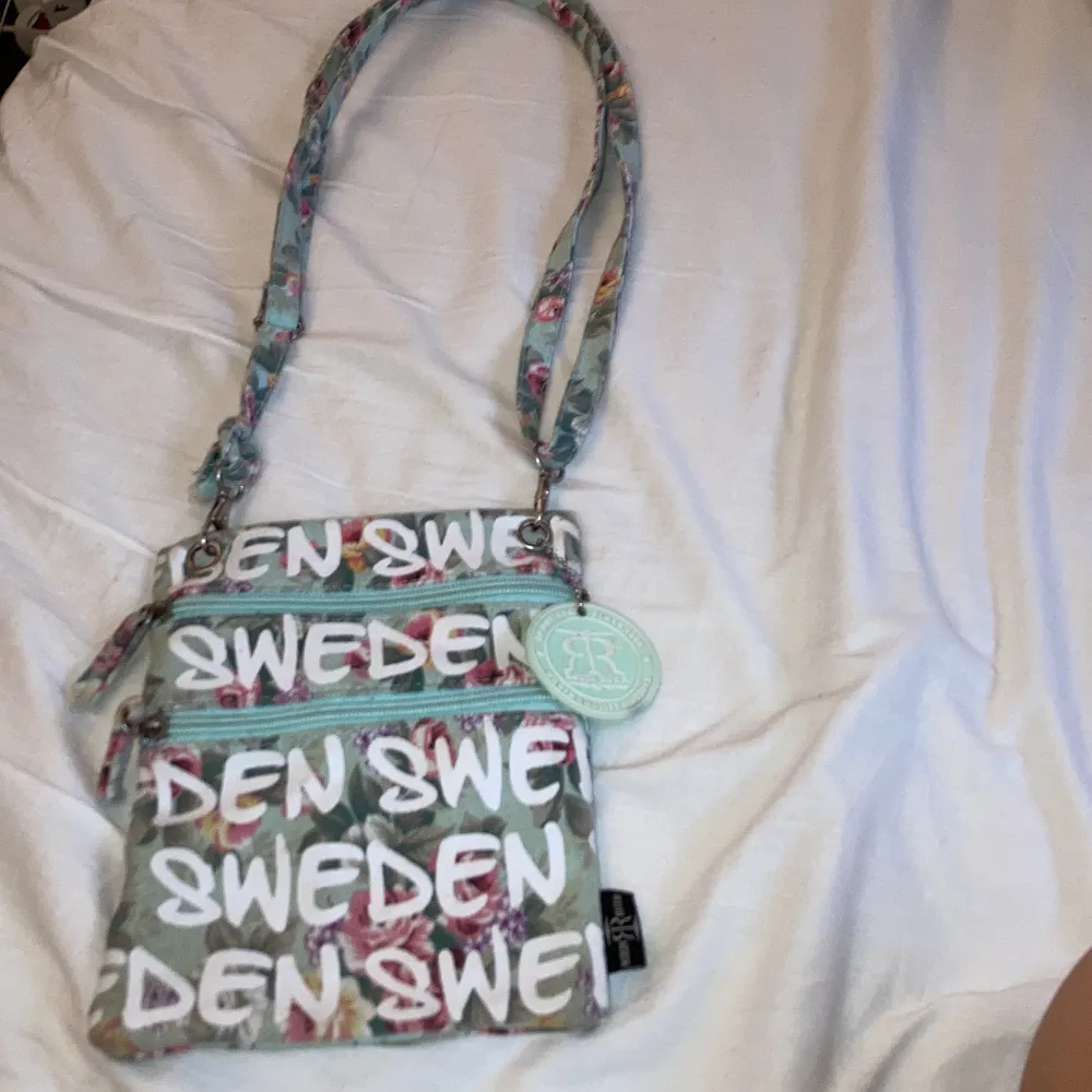 En handväska där du får plays med mycket, det är två pack ett stort och ett litet, det går att fixa Axel bandet mindre och större. Det är blommor och står den sweden på den. Den är turkos,rosa,vit.. Väskor.