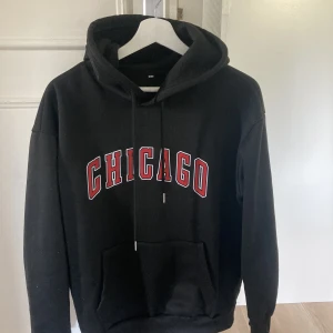 Hoodie med tryck på bröstet - En svart hoodie med en röd ”Chicago” text på bröstet, lite liten i storleken så skulle mer säga att det är storlek S istället för M