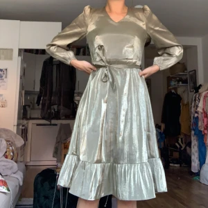 Festlig klänning - Klänningens färg framkommer ej till fullo på bild. Den är grön/guldig med skimmer i sig. Storleken är rymlig och går att anpassa tack vare bältet i midjan. Skulle säg att den passar även en 36a. Endast använd 2 gånger.