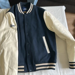 Mörkblå/ vit superdy store collegejacka  - Hej. Säljer min collegejacka då jag inte behöver den längre. Det finns ett litet hål vid den västra armen. Det är inte så synligt men det finns ändå där. 