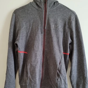 Hugo boss hoodie - Grå hoodie, detaljer av orange. Dragkedja. Fint skick. Finns tillhörande byxor.