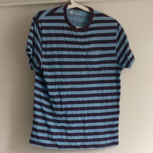 Blå randig t-shirt  - T-shirt med ljusblå-mörkblå ränder. Bra passform, bomull, ficka på bröstet.Köparen står för frakt
