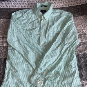 Randig gant skjorta - Denna skjortan är i bra skick och är använd fåtal gånger jag säljer denna skjortan eftersom att den är för liten för mig. Skjortan är randig med ljusgröna och vita smala ränder storleken är 158-164 centimeter och 13-14 år