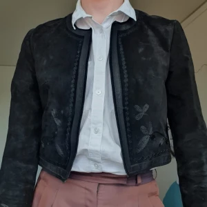 Kortjacka i Äkta Läder - Folkdräktsliknande överdel i svart mocka och läder med broderade blommor på framsidan. Mycket gott skick. 
