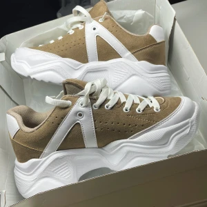 Nya Sneakers - Ett par helt nya Brun/Vita sneackrs. Säljer Pga fel storlek. Orginalkartongen är med. Den är i storlek 38 men passar nog även 37