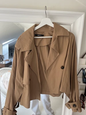 kort trenchcoat från ginatricot - den perfekta korta trenchcoaten! köpte den i storlek L för sitta lite större men passar alla från XS skulle jag säga! inte använd alls mycket!