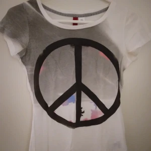 Vit kortärmad topp / T-shitt med stort Peace märke. Strlk: XS. Bomull, viskos? Felfri. - Vit kortärmad topp / T-shitt med stort Peace märke, köpt I Kanada. Strlk: XS. Bomull, viskos? Felfri.