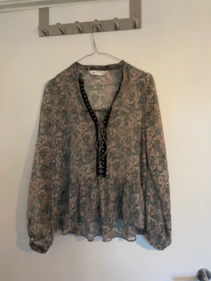 Blommig blus med fina detaljer  - Supersöt blus med volanger och knytningar. Helt oanvänd 