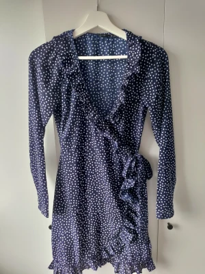 Blå prickig volang klänning - En blå prickig klänning med volanger. Har knyte i sidan. Kommer ifrån Ullared i storlek Xs.