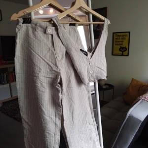 Striped beige set with cropped vest. - Randigt set med luftiga kostymbyxor och en croppad väst med cross-back design på ryggen. Knappt använda och säljes i mycket gott skick.