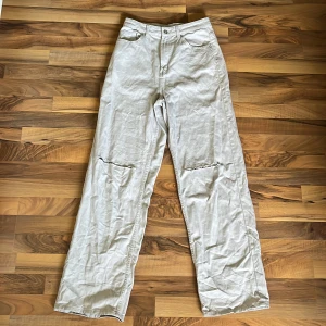 Baggy jeans - Supersnygga, beiga byxor med jeansliknande material. De är långa och vida med hål i benen. Är storlek 36 men skulle säga att de lutar mer åt 38. Helt oanvända så toppenskick!