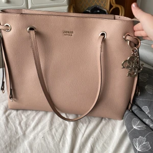 Äkta GUESS väska - En äkta GUESS väska köpt på Rizzo på Center Syd. Väskan är använd en del då den har varit skolväska en liten stund. Felfri förutom en liten söm på handtaget som är lite uppriven. Kan skickas omgående, pris kan diskuteras. Finns fler bilder om de önskas.