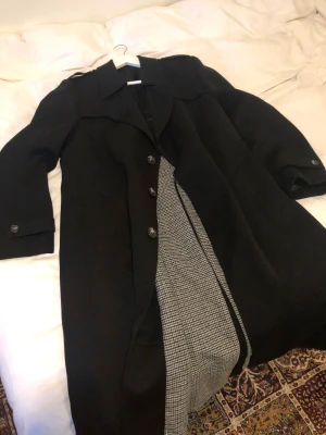 Lång svart trenchcoat Str 44 - Äkta vintage kappa från tyska märket Terminal, perfekt skick. Saknar dock skärp. Dubbelfodrad i både ylle och silke. Byst: 57cm. Längd från krage: 120cm. Dma gärna vid frågor eller funderingar. Köparen står för frakt.