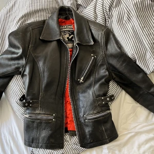 Skinnjacka bikermodell - Riktigt snygg rejäl skinnjacka i superbra skick - Inga hål eller dylikt, bara snygg patina. Modellen på bilden är strl s för referens. Har resår i ryggen men hyfsat rak modell. Fina knäppningsdetaljer och många fickor. 