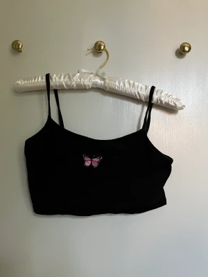 Topp -  En svart topp från SHEIN med en rosa lila fjäril i mitten är i storlek 152 men passar för de som har storlek XS till S 