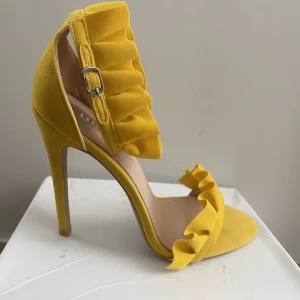 Gula klackar  - Säljer ett par frill detailed heels in yellow faux suede. Oanvända 