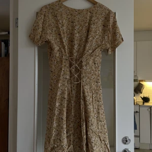 Sommarklänning - Gulblommig sommarklänning med corsetdetalj på ryggen!