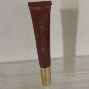 Max Factor Colour Elixir Lip Cushion Gloss  -  ett vårdande läppstift designat för att passa till alla tillfällen. Formulan är full av skyddande antioxidanter och E-vitamin, ger ett naturligt resultat med en fin glans. I nyansen Nude glory.  Kan även postas med frimärke/portokod för 15:-
