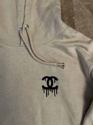 Jackie hoodie med chanel märke på bröstet.  - Begie hoodie från jackie med chanel tryck på bröstet. (Inte äkta Chanel) 