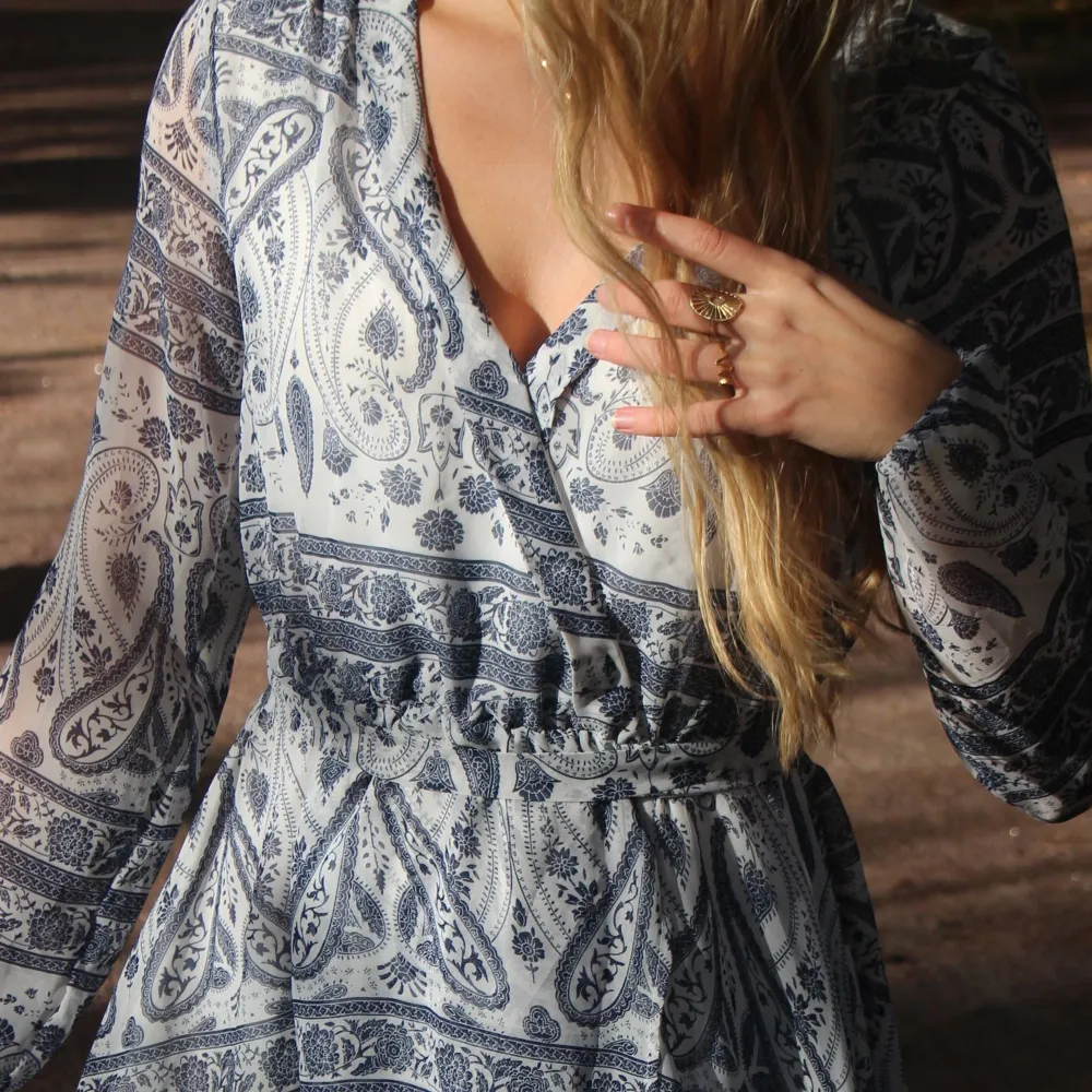 Beställningar görs via vår hemsida: thrifteddesign.one.   En blåmönstrad långärmad klänning med band runt midjan. . Klänningar.
