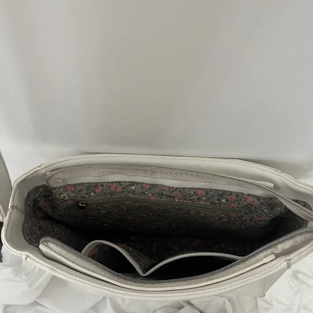 En vit väska i ungefär 25 cm i bredd, 20 cm hög och 10 cm djup.  Använts i ett år och är då i begagnat skick med små defekter i fake lädret, kedjor funkar.  Köpt från Gekås  🌟🫶🤍. Väskor.