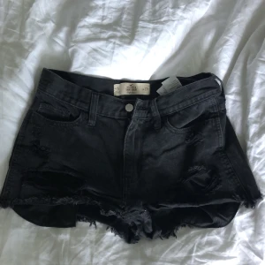 Svarta jeansshorts - Högmidjade jeansshorts från Hollister med slitningar i storlek w27.