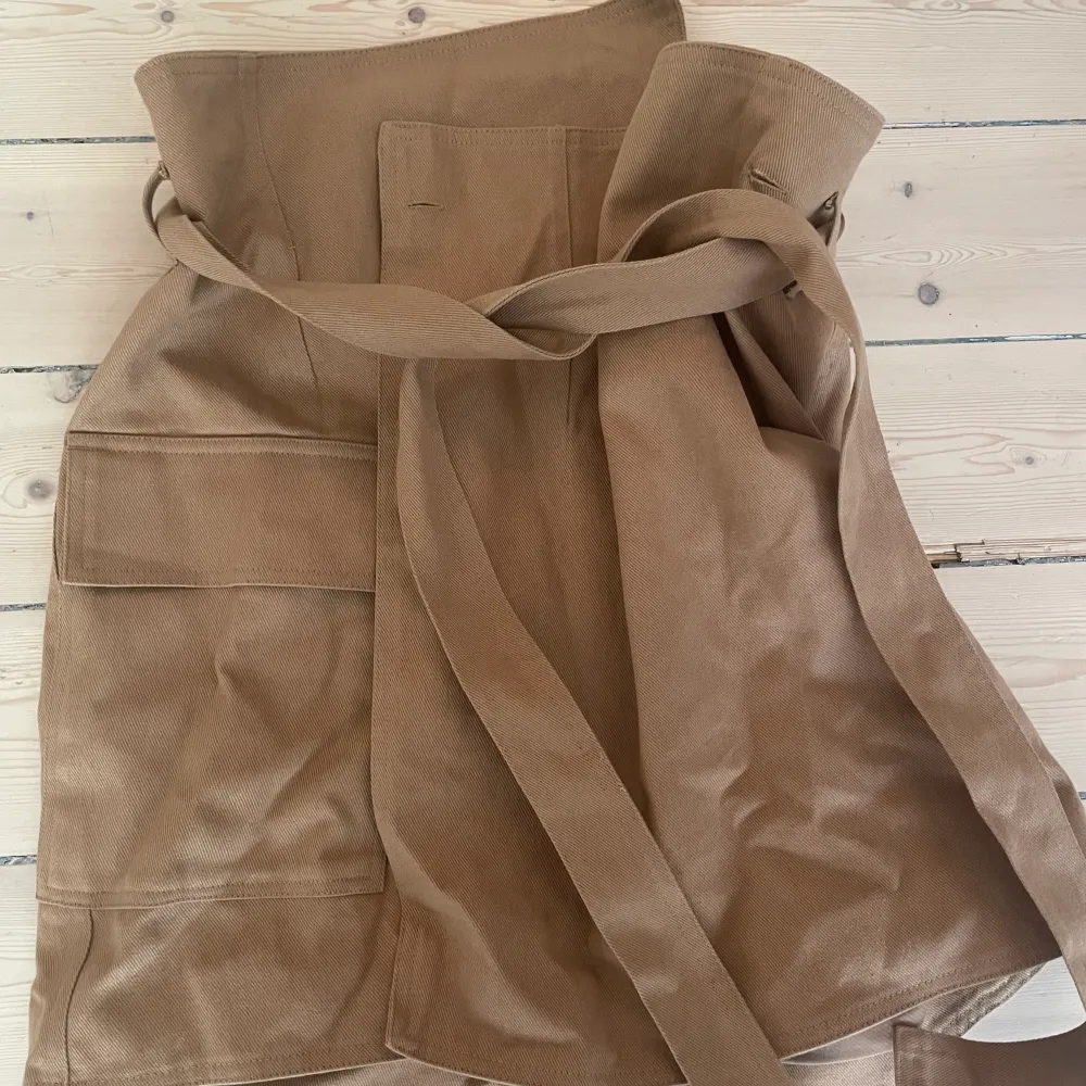Fin beige/brun kjol med knapp och bälte från HM Helt oanvänd med prislappen kvar. Storlek: 36 100% bomull . Kjolar.