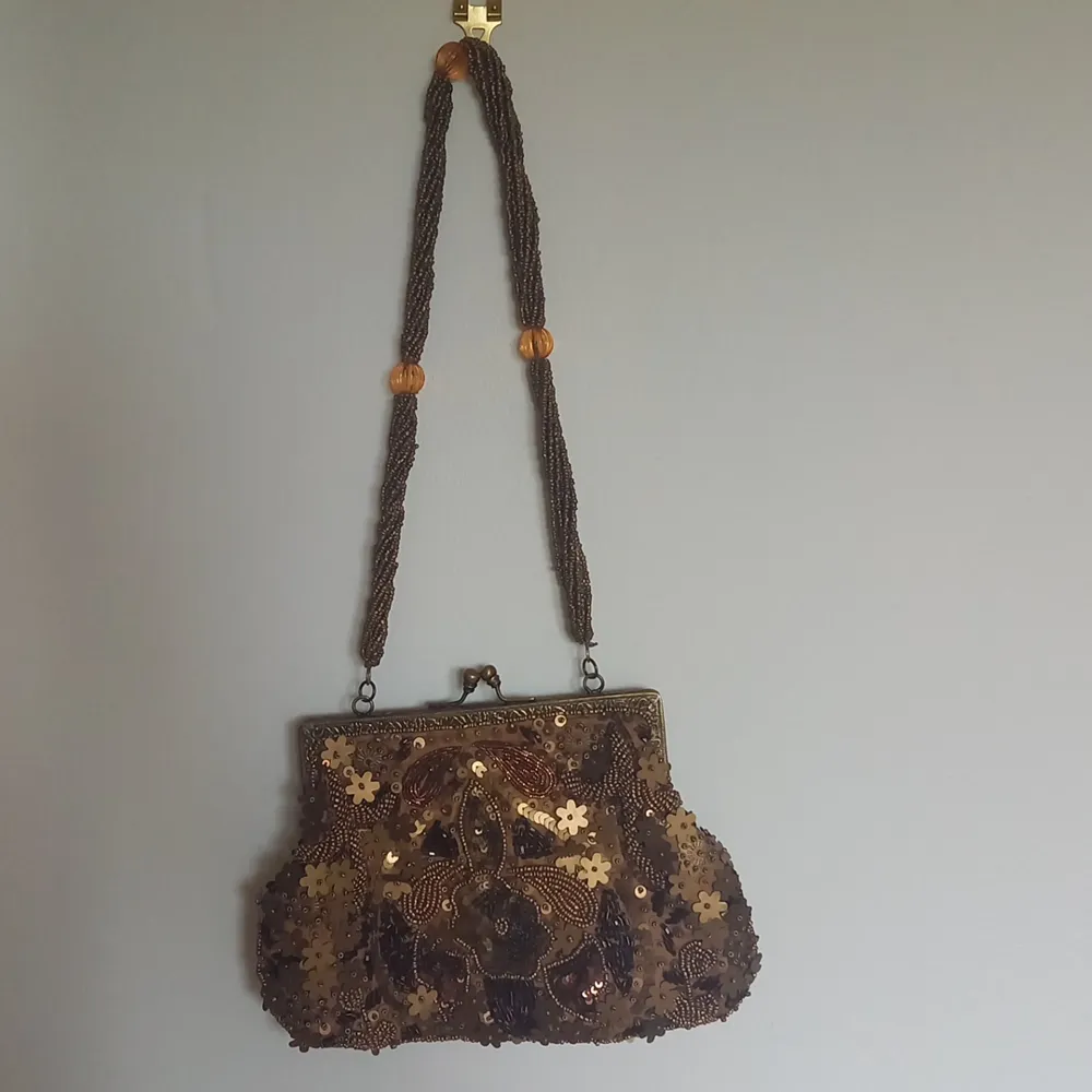 A bronze/gold beaded purse with metal clasp opening. 15.5cm openning fits phone, wallet and any other smaller essentials. The shoulder strap is about 26cm long. Slight damage inside purse where bit of linning fell off, can be seen in third picture.. Väskor.