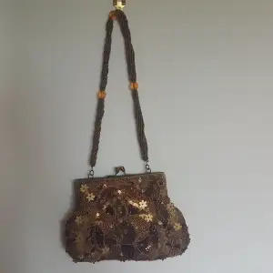 A bronze/gold beaded purse with metal clasp opening. 15.5cm openning fits phone, wallet and any other smaller essentials. The shoulder strap is about 26cm long. Slight damage inside purse where bit of linning fell off, can be seen in third picture.