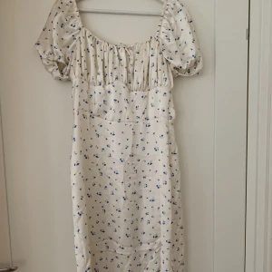 Sommarklänning  - Vit sommarklänning med blåa blommor på i satin! Från NA-KD i storlek 42. 