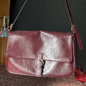 Väska - Skitsnygg väska i en bra storlek, fint skick. Väskan har justerbart mindre band, samt ett längre axelband (se andra bild). Färgen stämmer med bild - vinröd.