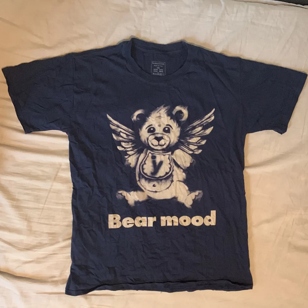 Marinblå t-shirt med en nallebjörn på med ängel vingar. Bra skick förutom ett litet hål vid ryggen som knappt är synligt. Material: 100% bomull. T-shirts.