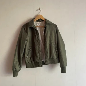 Retro vårjacka med krage - Cool grön bomberjacka med krage och fint randigt foder. Säljes då den blivit för liten för mig. I utmärkt skick.  Storlek S. 