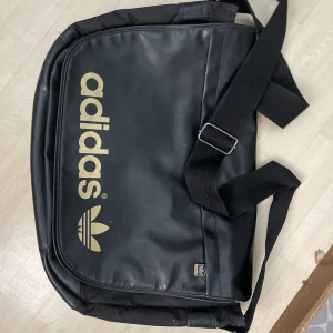 O använd adidas väska  - O använd adidas svart/guld väska med 2facks förvaring 