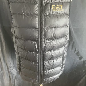 Tunn täckväst från EA7 - Original EA7, svart väst i bra använt skick. Strl 14A-160cm.  2 små skav. 