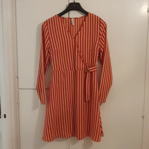 Randit klänning - Beige och röd randig klänning med detalj i midjan.