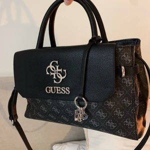 Guess väska - En svart guess väska med mörkgrå detaljer. Det har en axelrem man kan ta på och av! Väldigt rymlig och snygg. Har använt den cirka några gånger så är i väldigt bra skick! Köpte den sommaren 2020. Kosta nypris 149 €/ 1519kr 