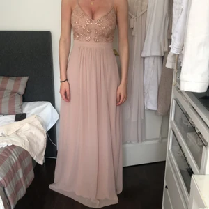 Nellyeve balklänning i rosa - Lång balklänning i ljusrosa med smyckesdetaljer vid bysten. Klänningen är i storlek 36 och har en slid vänster ben 