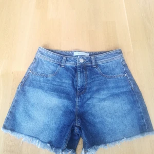 Jeansshorts oanvända  - Oanvända, mörkblåa jeansshorts i storlek 38 med fransar nedtill. Fejkfickor fram men riktiga baktill