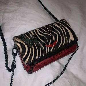 Zadig Voltaire väska - Unik liten Zadig Voltaire väska med zebramönster, röda/gröna partier och silvriga detaljer! Piffar upp en tråkig outfit och är perfekt när man inte behöver så mycket grejer med sig. Den är väl använd men ändå i fint skick!
