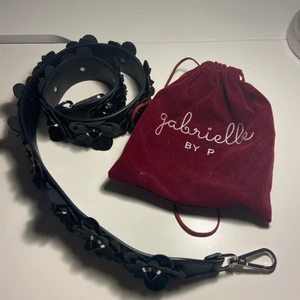 Väskband black blossom - Hej, säljer ett oanvänt black blossom väskband från Gabrielle by P då den inte kommer till användning. Den är 105 cm lång med svart blommor längs med hela bandet, fästs i väskan med silver spännen. Orginalpåsen är kvar! Skriv vid intresse!❤️